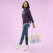 Full-body lifestyle shot of a model holding the Loungefly Disney Stitch & Angel True Love tote bag with pastel artwork and light blue handles.