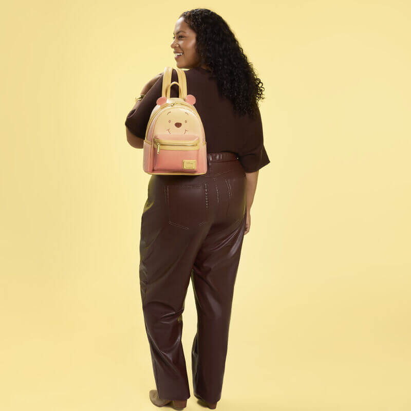 Model wearing the Loungefly Disney Winnie the Pooh glitter mini backpack on a yellow background