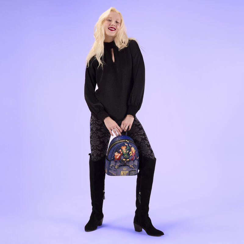 Model holding the Loungefly Hocus Pocus Sanderson Sisters mini backpack against a lilac backdrop
