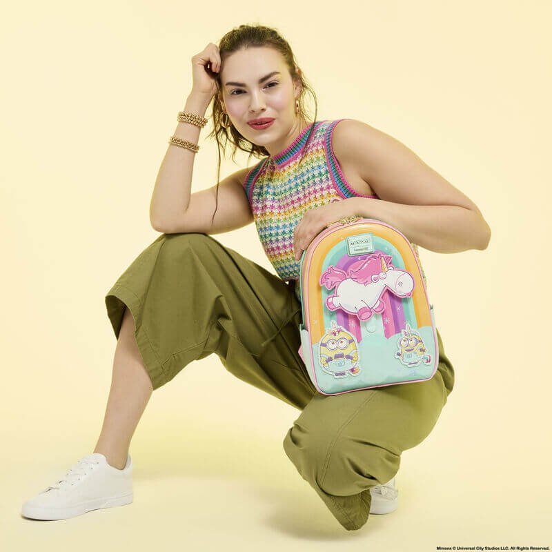 Model holding Loungefly Minions Fluffy Unicorn mini backpack; oversized unicorn appliqué pops against rainbow background – Loungefly bag

