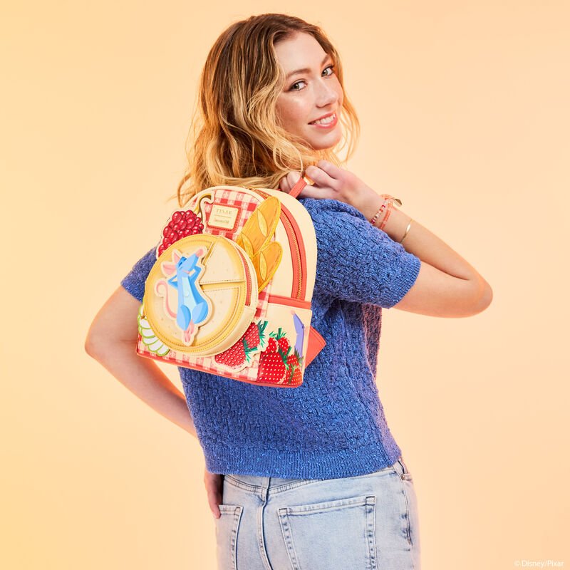 Model wearing the Loungefly Ratatouille Remy Cheese Wheel Mini Backpack on shoulder, peach background