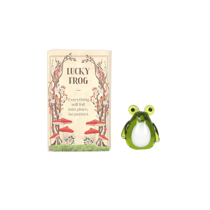 Mini green glass lucky frog pocket charm beside illustrated woodland matchbox reading ‘Everything will fall into place’.

