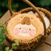 Capybara Lu plush pouch resting in a wicker basket, highlighting fluffy mustard fur and stitched face.
