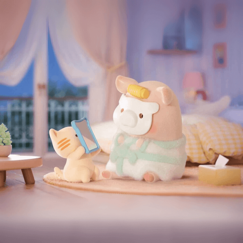 Lulu the Piggy Home Life blind box “Spa Day” figure—pig in robe and face mask admired by cat holding mirror in bedroom.
