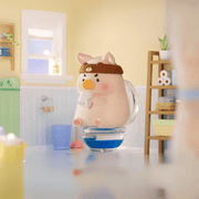 Lulu the Piggy Home Life blind box “Tea Break” figure—pig sipping from mug while seated on a clear toilet tank in light-filled bathroom.









