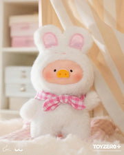 Lulu the Piggy Joyful Time blind box plush in snow-white bunny suit with pink gingham bow, resting on fluffy bedding.

