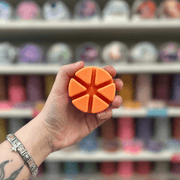 Orange segmented wax melt held in hand with a colourful wax melt shelf in the background