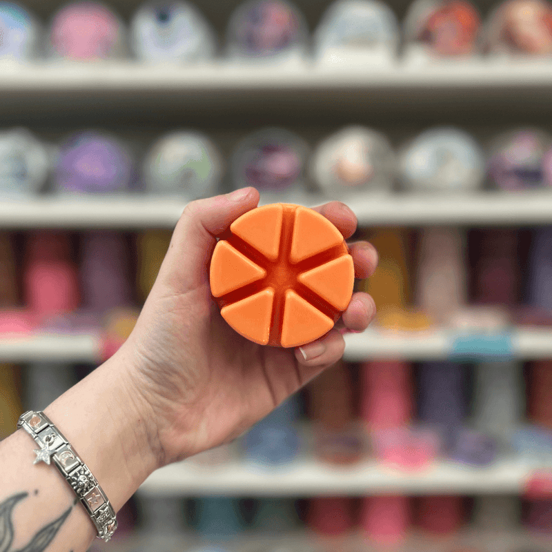 Orange segmented wax melt held in hand with a colourful wax melt shelf in the background