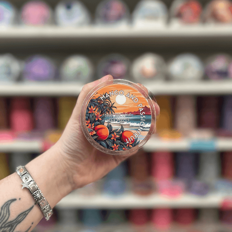 Mango and Passionfruit wax melt pot held in hand in front of a bright wax melt display