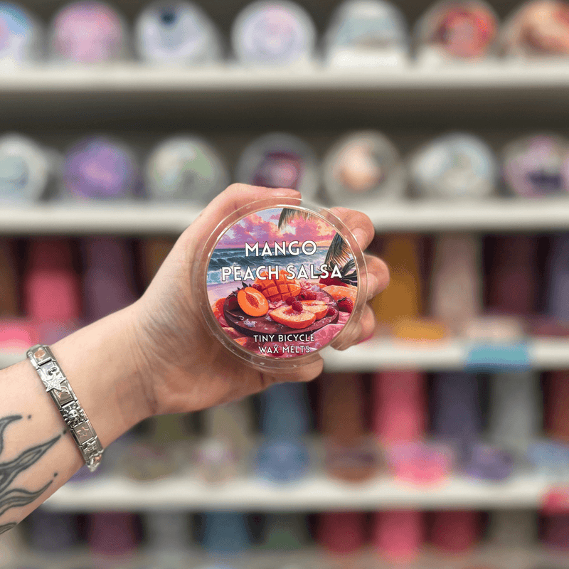 Mango Peach Salsa wax melt pot held in hand with colourful wax melt display in the background