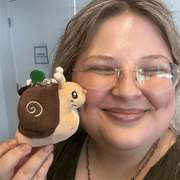 Person holding Micro Squishable Garden Snail plush keychain beside their face to show its miniature size