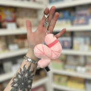 Micro Squishable Worm Keychain plush in pale pink with a metal clip, held in a gift shop setting