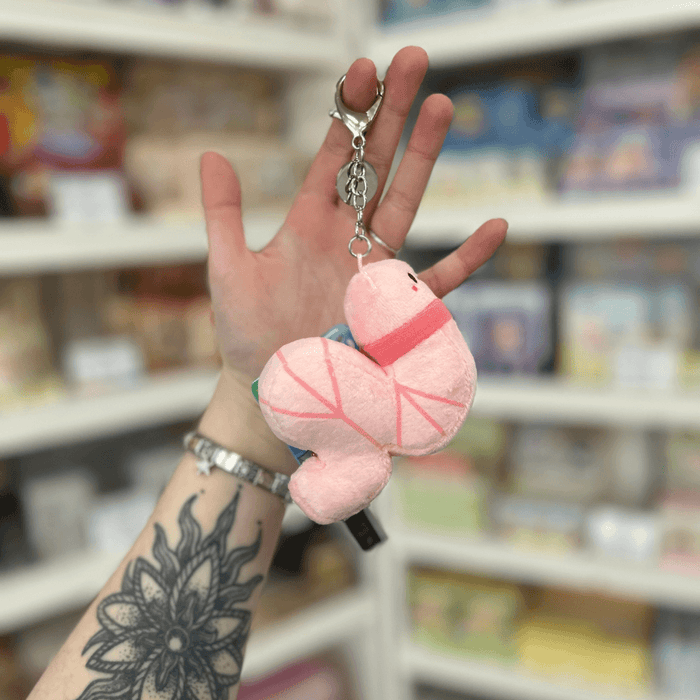 Micro Squishable Worm Keychain plush in pale pink with a metal clip, held in a gift shop setting