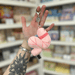 Micro Squishable Worm Keychain plush in pale pink with a metal clip, held in a gift shop setting