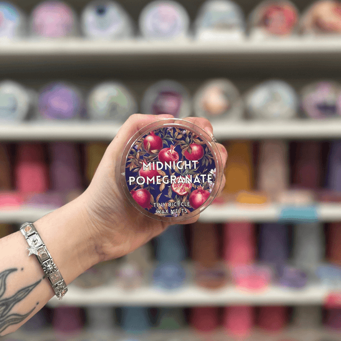 Midnight Pomegranate wax melt pot held in hand with colourful wax melt display in the background