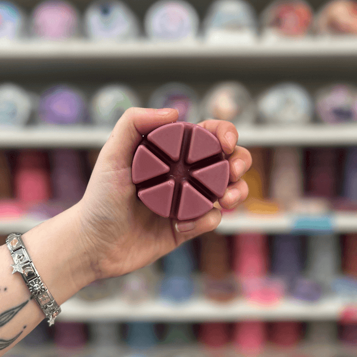 Midnight Pomegranate wax melt segments held in hand with colourful wax melt display in the background