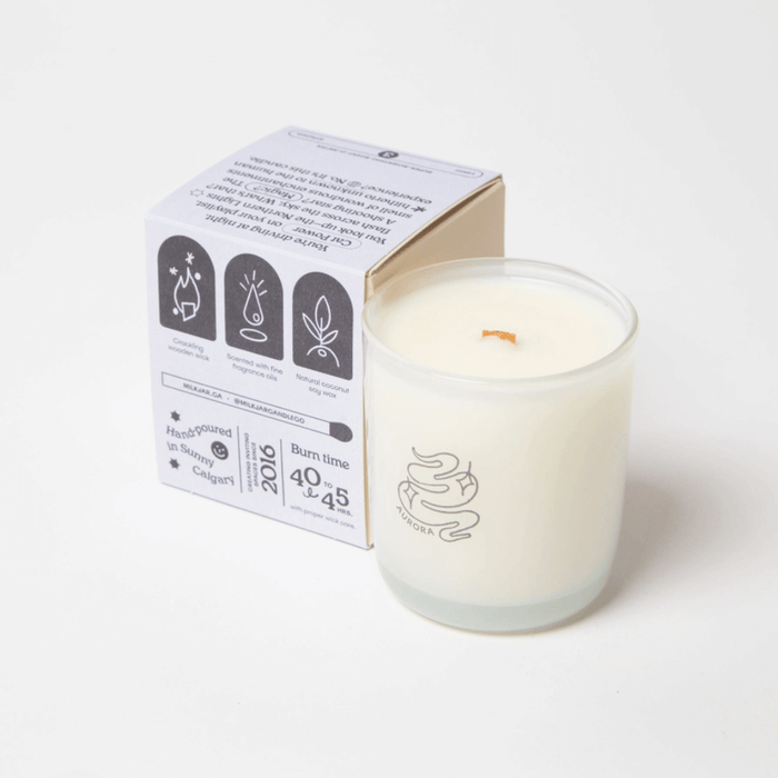 Milkjar Aurora candle beside the box showing icons for wooden wick, fragrance oils and coconut soy wax.