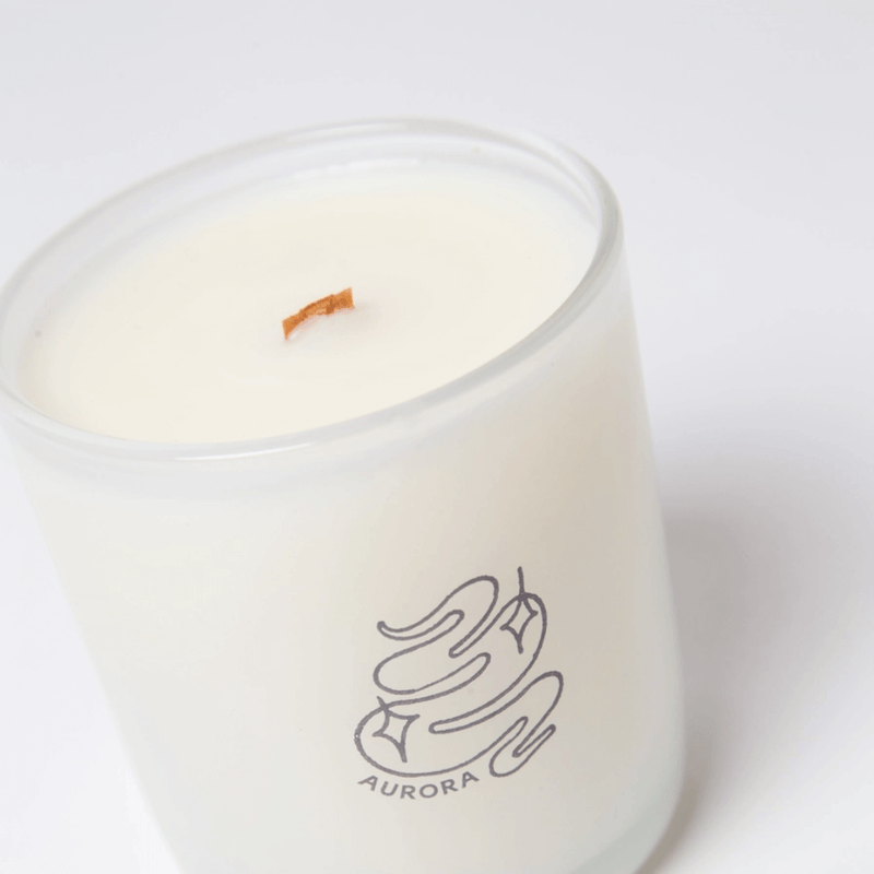 Close-up of Milkjar Aurora candle in frosted glass with wooden wick and Aurora logo.