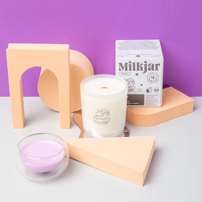 Styled product photo of Milkjar Aurora candle and box on a purple background with peach props.