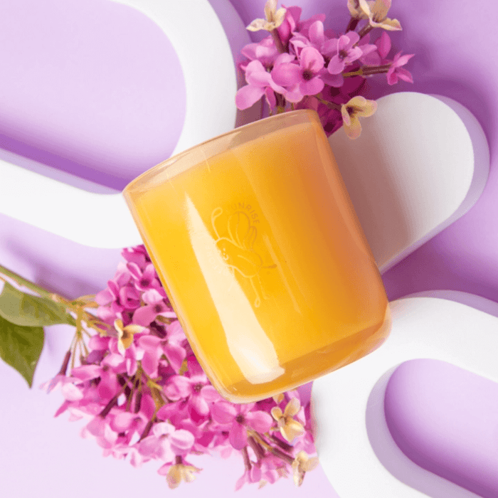 Amber Milkjar Before Sunrise candle styled with pink flowers on a purple background