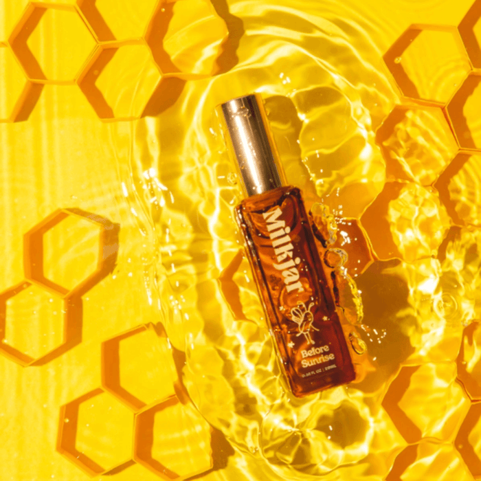 Milkjar Before Sunrise perfume roller bottle in water splash on yellow honeycomb backdrop
