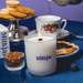 Close-up of lit Milkjar Blueberry Tea coconut soy candle with crackling wooden wick on a tea table with teacup and treats.