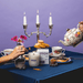 Milkjar Blueberry Tea coconut soy candle with wooden wick on a tea table with floral teacups, teapot, cookies and jam toast.