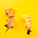Hands holding an orange and Milkjar Citrus candle through torn yellow paper, bright yellow backdrop.
