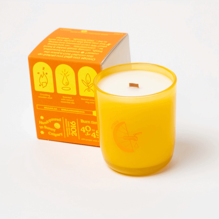 Milkjar Citrus candle beside box showing icons for wooden wick, essential oils and coconut soy wax.