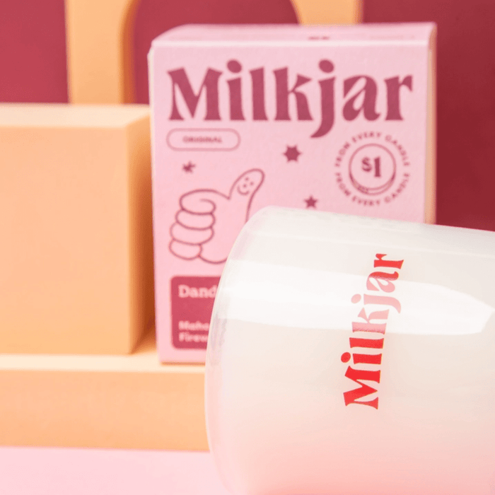 Close-up of Milkjar candle glass with branding, with the Milkjar Dandy box softly focused in the background.