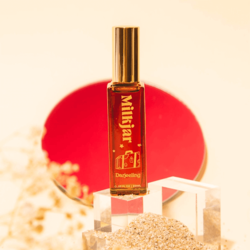 Milkjar Darjeeling perfume roller standing on clear blocks with red circle backdrop and warm styling