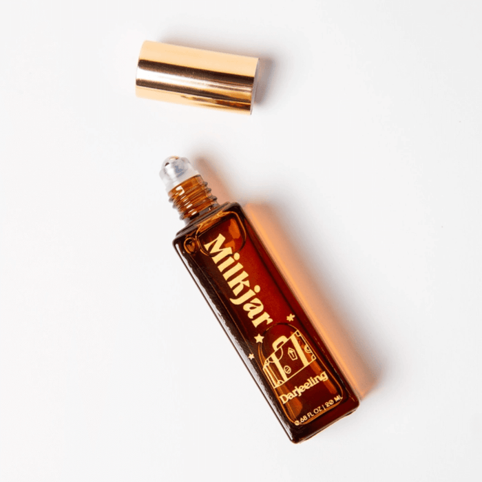 Milkjar Darjeeling Patchouli & Santal perfume roller lying open with cap above on a white background