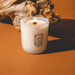 Lit Milkjar Golden Hour candle in frosted glass with wooden wick and hourglass logo.