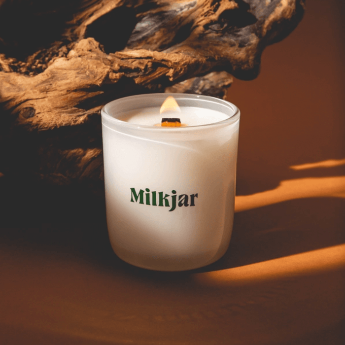 Lit Milkjar candle in frosted glass with wooden wick, styled with warm wood tones in the background.
