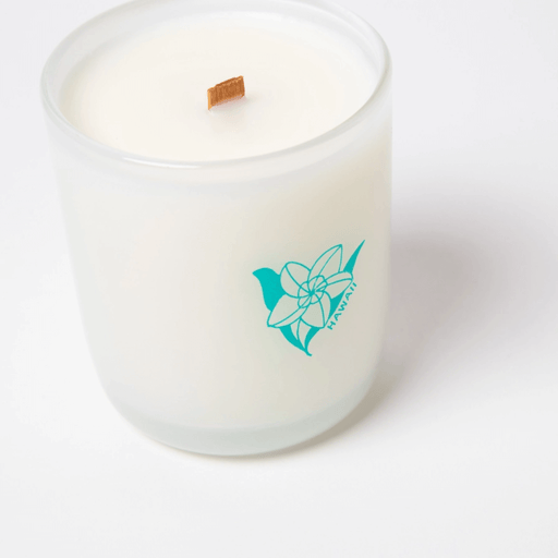 Close-up of Milkjar Hawaii candle showing the wooden wick and teal flower logo on frosted glass.