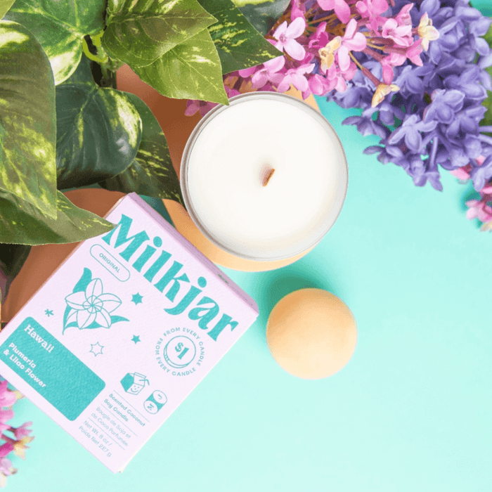 Top-down flatlay of Milkjar Hawaii candle with box, flowers and pastel props on a turquoise background.