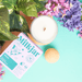 Top-down flatlay of Milkjar Hawaii candle with box, flowers and pastel props on a turquoise background.