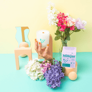 Milkjar Hawaii candle styled with colourful flowers, pastel props and a hand holding the frosted glass candle.