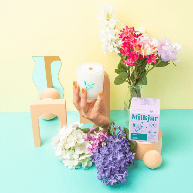 Milkjar Hawaii candle styled with colourful flowers, pastel props and a hand holding the frosted glass candle.