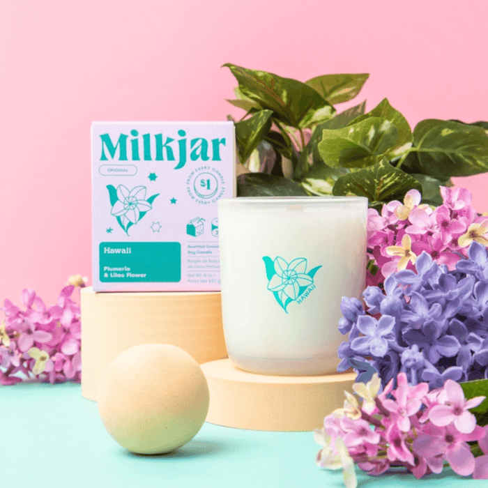 Milkjar Hawaii candle and box styled with lilac and pink flowers on a pastel pink background.