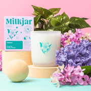Milkjar Hawaii candle and box styled with lilac and pink flowers on a pastel pink background.