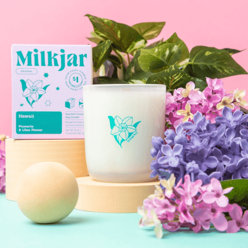 Milkjar Hawaii candle and box styled with lilac and pink flowers on a pastel pink background.