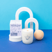 Milkjar Hygge candle with teapot icon on the glass beside the Hygge box on a blue backdrop with modern arch props.