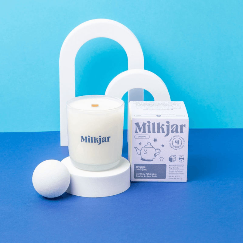 Milkjar Hygge coconut soy candle and box styled on a bright blue set with minimalist arch props and a wooden wick.
