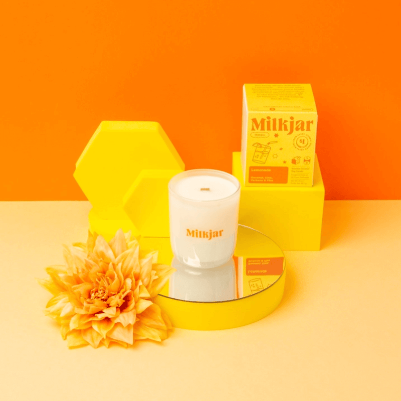 Milkjar Lemonade candle with lemonade icon on a bright yellow set with the box and a yellow flower.