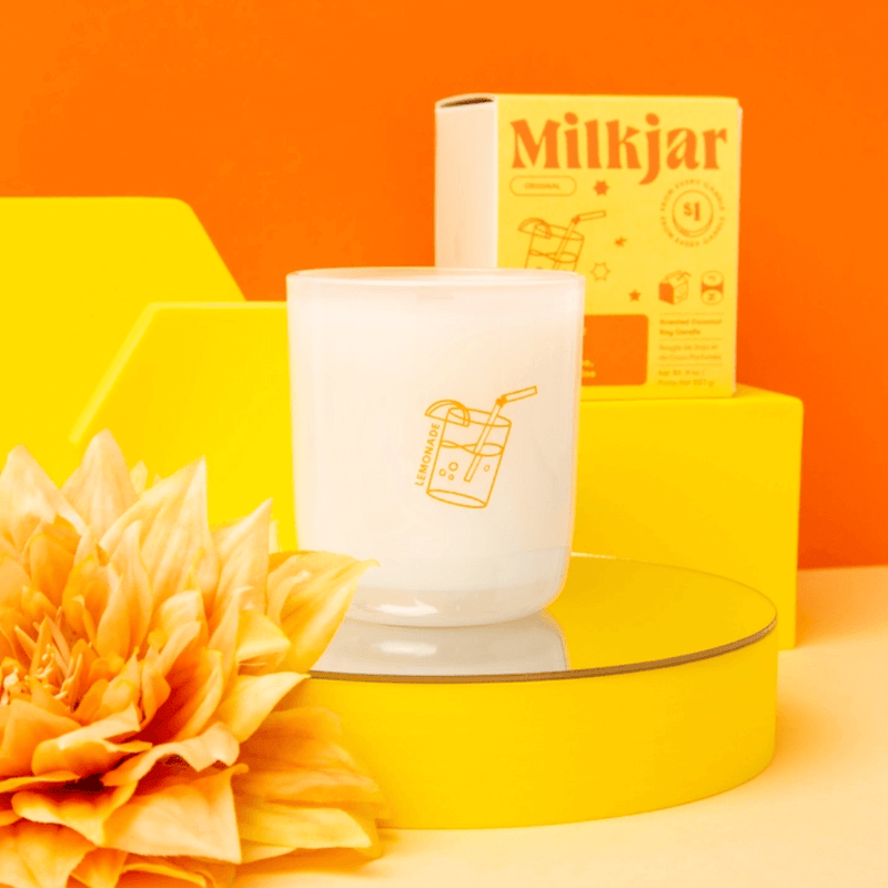 Milkjar Lemonade candle beside the box showing icons for wooden wick, fragrance oils and coconut soy wax.