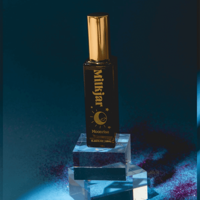 Milkjar Moonrise Neroli & Plum perfume roller standing on clear acrylic blocks with moody blue background