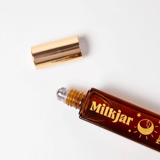 Milkjar Moonrise perfume roller lying open with cap beside bottle on a white background