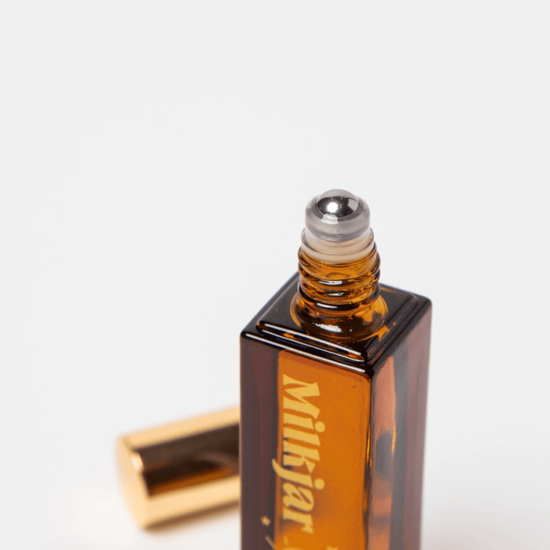 Close-up of Milkjar Moonrise perfume rollerball top on amber glass bottle with gold cap in background