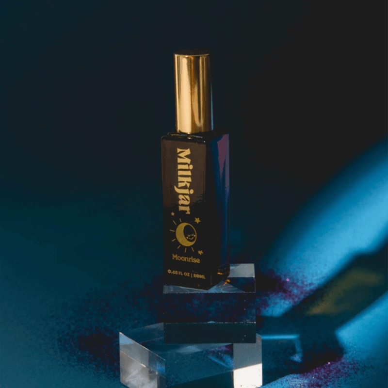 Styled Milkjar Moonrise perfume roller on acrylic blocks with dark blue lighting and purple glitter accents